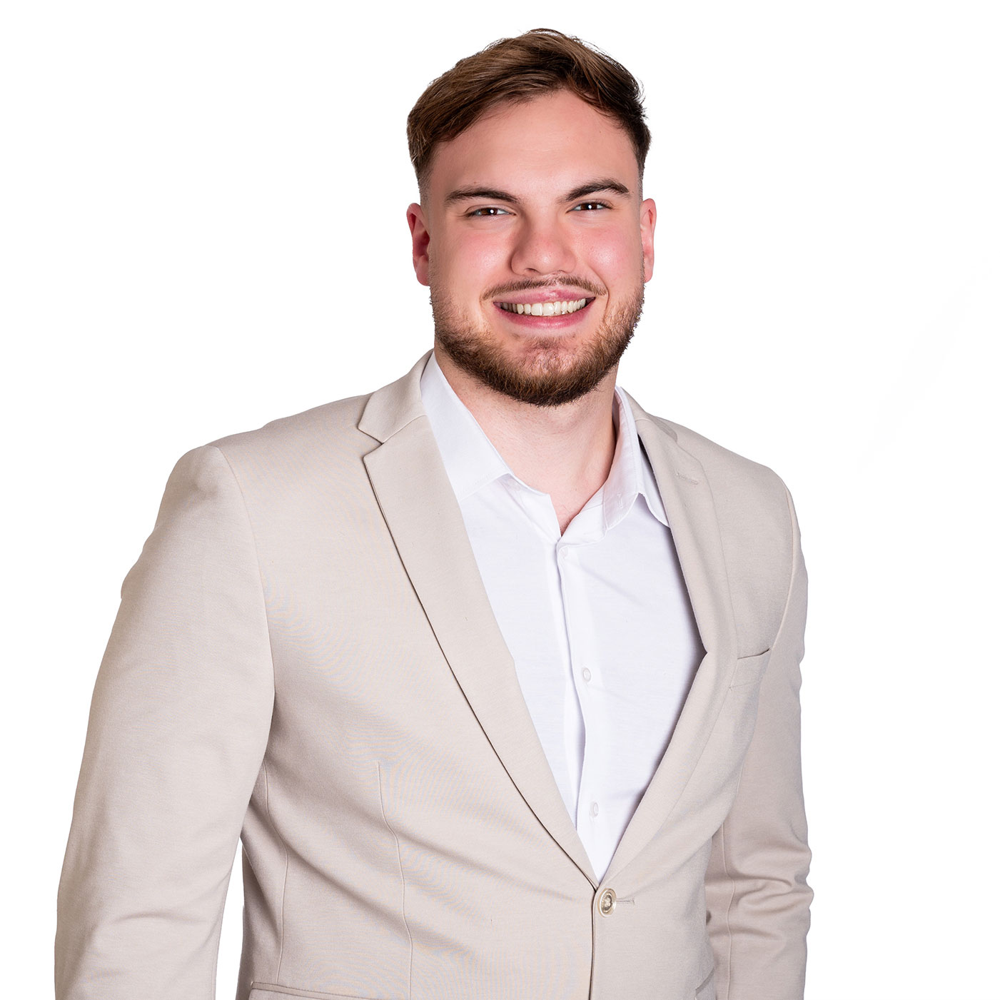 Freundliches Business-Porträt eines jungen Mannes in hellem Sakko und weißem Hemd vor weißem Hintergrund, mit lockerer Haltung und offenem Lächeln.